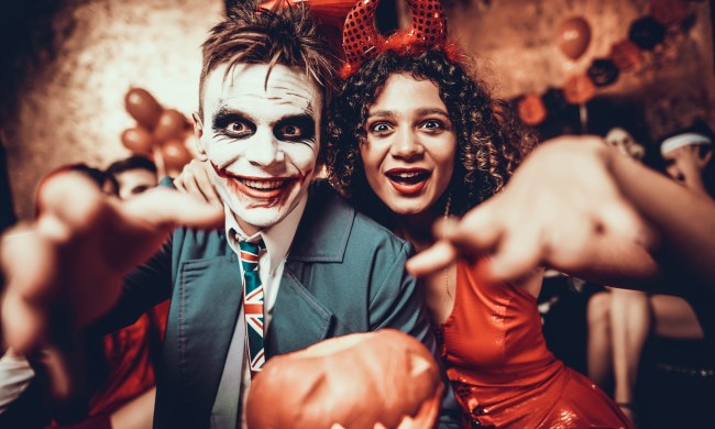 Portrait of Young Couple in Halloween Costumes. Beautiful Woman and Handsome Young Man Wearing Costumes holding Pumpkin at Halloween Party in Nightclub. Happy Friends having Fun Celebrating Halloween